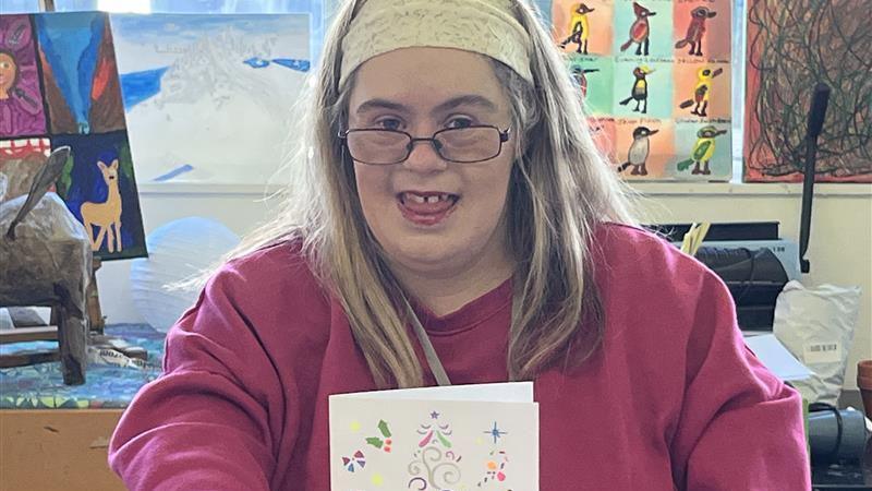 A young woman dressed in pink is holding a Christmas card she's made