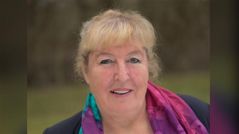A headshot of a blonde woman wearing a colourful scarf.