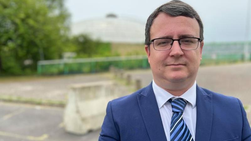 Swindon Conservative councillor Daniel Adams wearing a blazer and tie standing in front of the closed Oasis leisure centre.