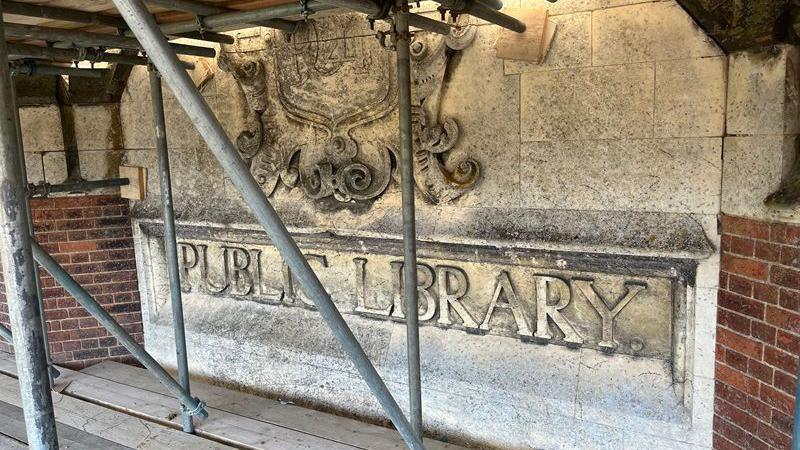 Scaffolding in front of a stone public library sign