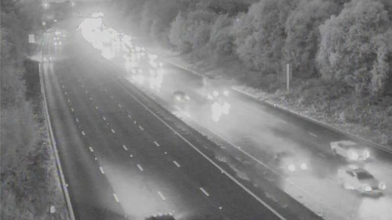 A motorway from above is captured in black and white. Substantial traffic is seen travelling in one direction.