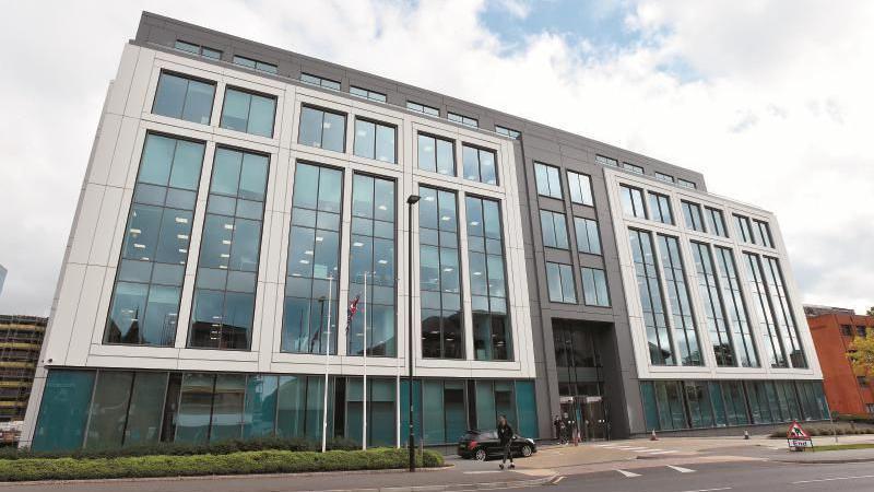 Slough Borough Council's headquarters, a large modern building predominantly fronted with glazing and white walls. It's a sunny day and the sky is blue.