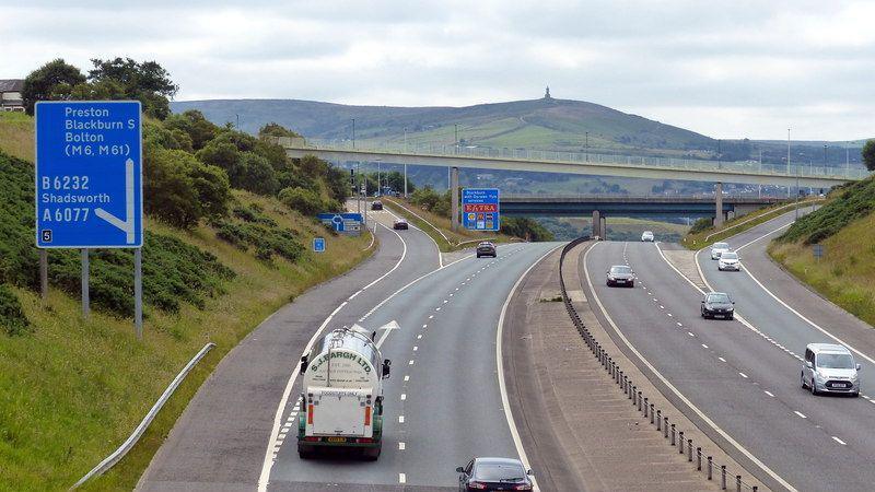 Vehicles on either side of the M65 at a slip road junction, with Darwen Hill and the Jubilee Tower on the summit in the background