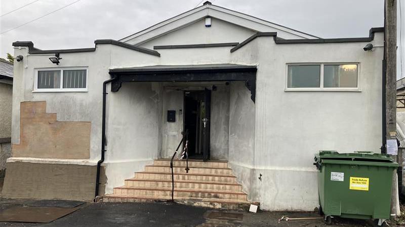 A building with a white exterior and steps leading up to a central door. The building is lightly charred with smoke damage on the exterior.