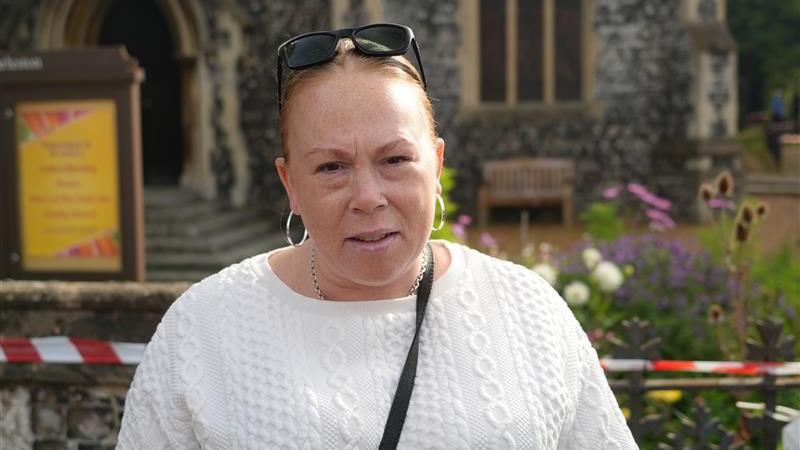 A woman wearing a white jumper with sunglasses on her head. She is looking at the camera 