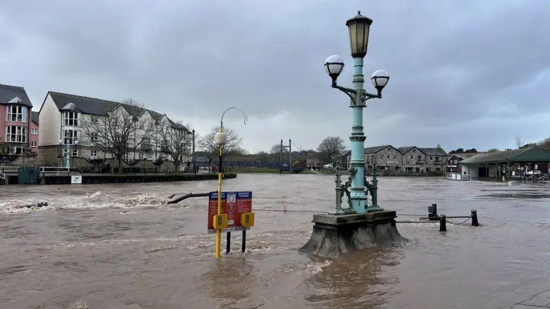 River water floods a street with water seen lapping around a lamppost.