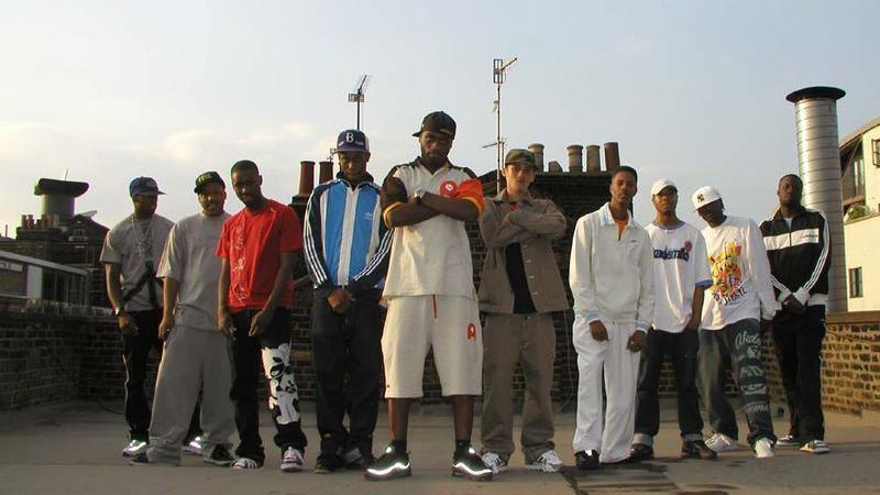 The 10 MCs from Pow! pose on a rooftop while facing the camera, a metal chimney can be seen behind them to the right hand side