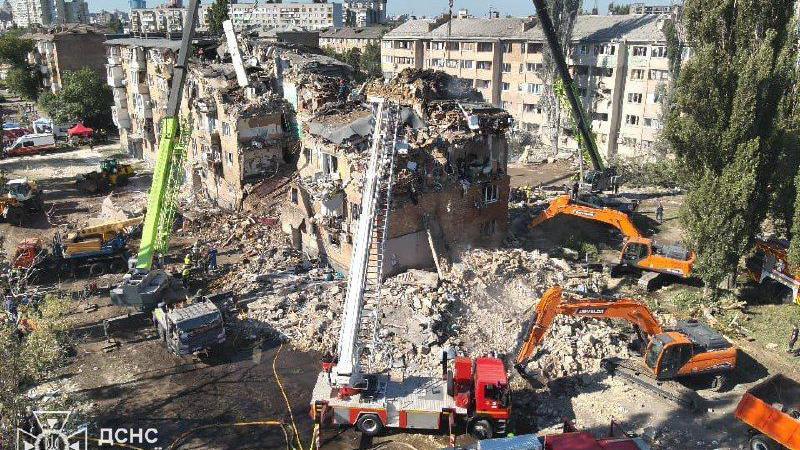 A building torn apart by Russia bombs surrounded by rescue vehicles