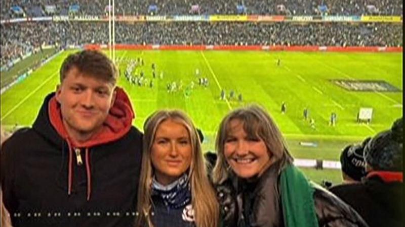 Liz Steele with son Paddy and another woman, standing in the crowd at a rugby game. Their backs are to the pitch as they smile for the camera.All three are smiling while wearing jackets and hoodies for the weather.