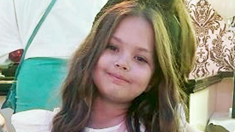 A young girl with long dark hair smiles at the camera.