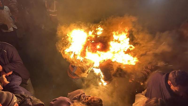 A flaming barrel with people leaning away from it.