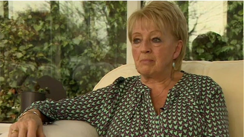 Doreen Soulsby is sitting in an armchair wearing a green and brown shirt with love hearts on it and looking unsmilingly away from the camera 