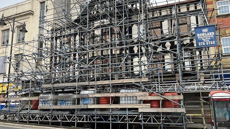 Scaffolding obscures the view of a black-and-white Tudor-inspired facade