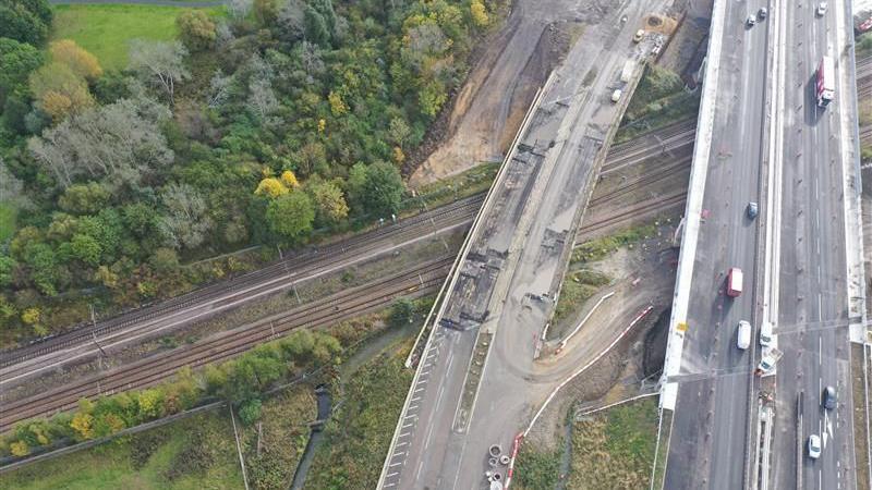 The picture shows an aerial image of an old bridge, no longer in use with a new one next to it. Both cross a railway line