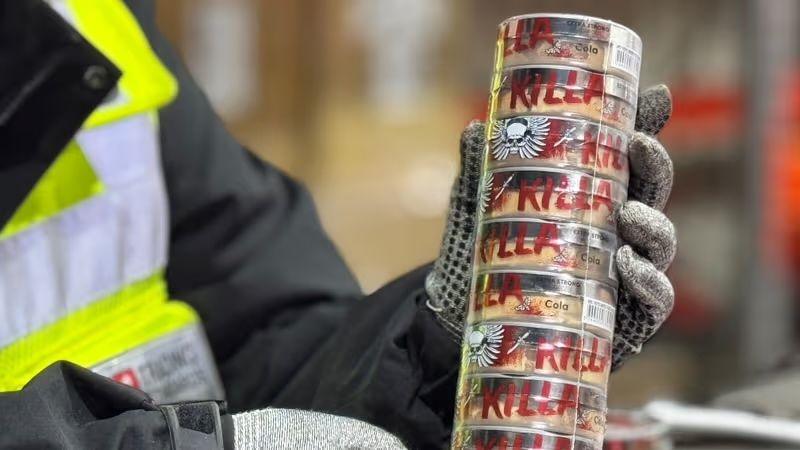 Gloved hands hold a stack of tubs of nicotine pouches labelled with the word Killa