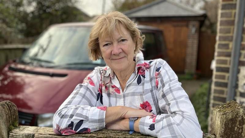 Jane Francis leaning on her garden gate in front of her cottage near the Cuckmere River