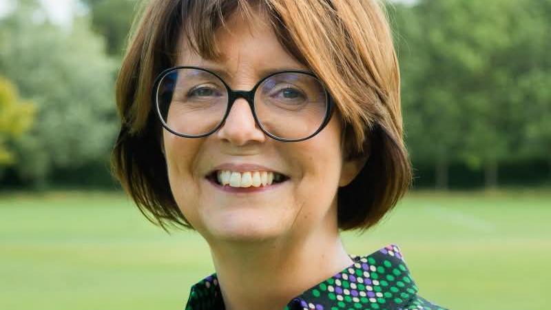 A woman with light brown hair and glasses smiles into the camera.