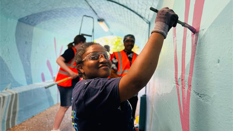 Sheryl is painting a red streak on the wall with paint clear glasses covering her eyes.