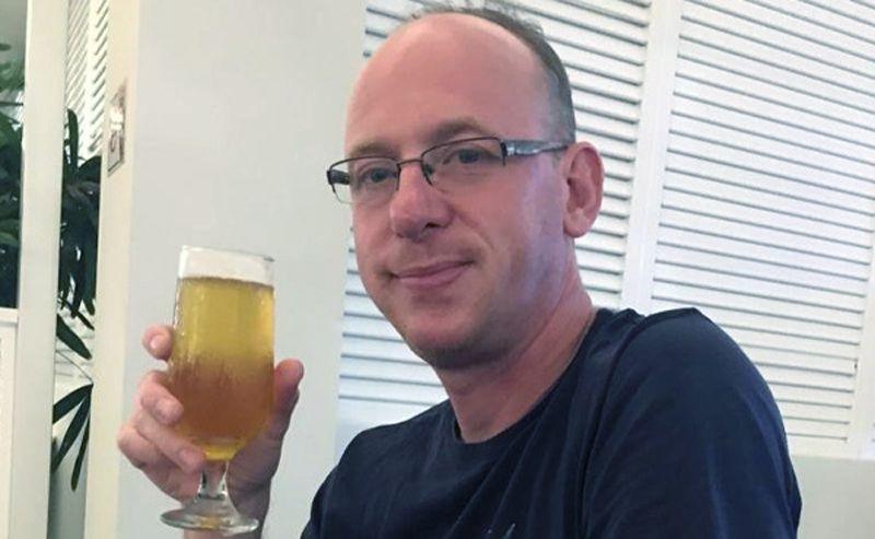 A man in glasses and dark shirt holding a beer.