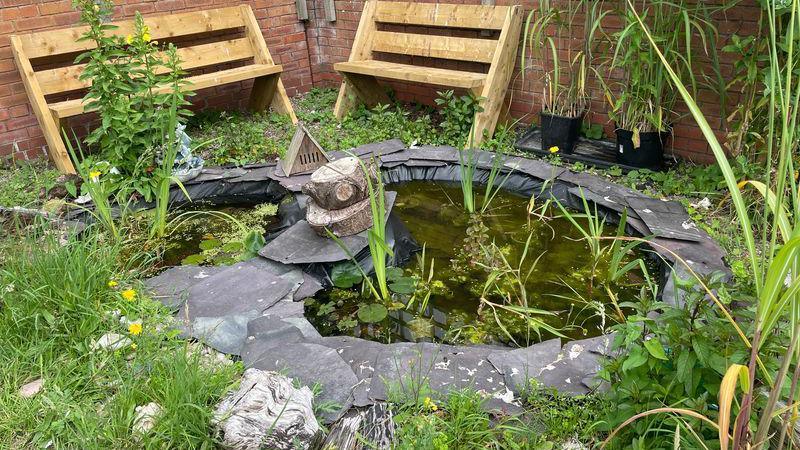 A pond surrounded by slate and plants with chairs in the background