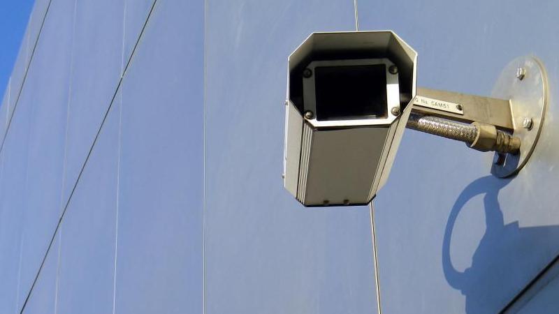 A silver CCTV camera is attached to a silver metal wall. 