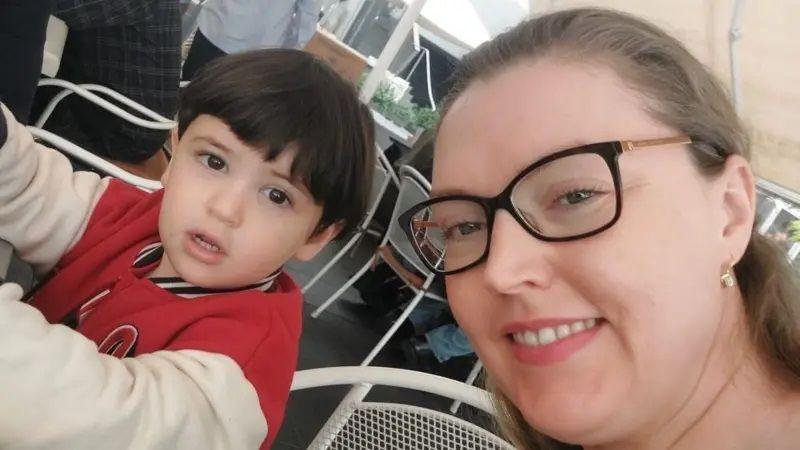 Catherine Flanagan with her son David. David has black hair and is wearing a red and white jacket, Catherine has light brown hair tied back and is wearing glasses. They are sitting at an outdoor table at a cafe  