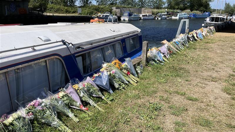 Boats on the river in Beccles with floral tributes left alongside the river.