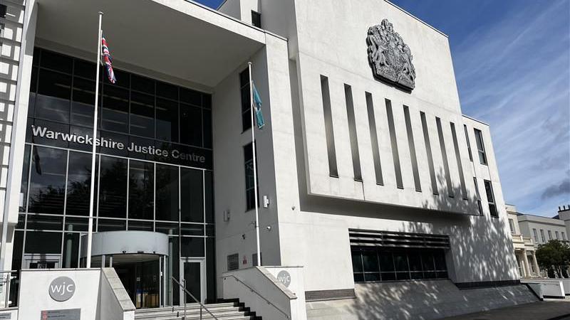 An exterior shot of a courthouse. The building is white and has steps leading up to it. It has a sign that reads "Warwick Justice Centre".