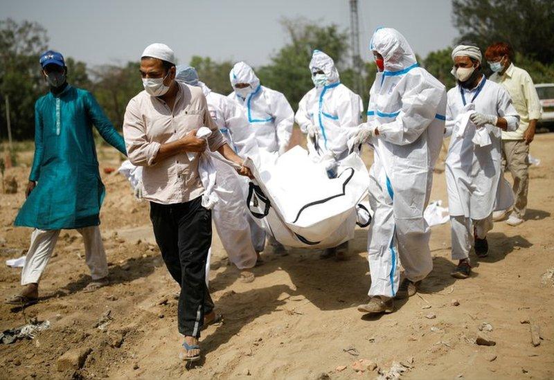 Masked relatives carry the shrouded corpse of a Covid victim through a Delhi graveyard.