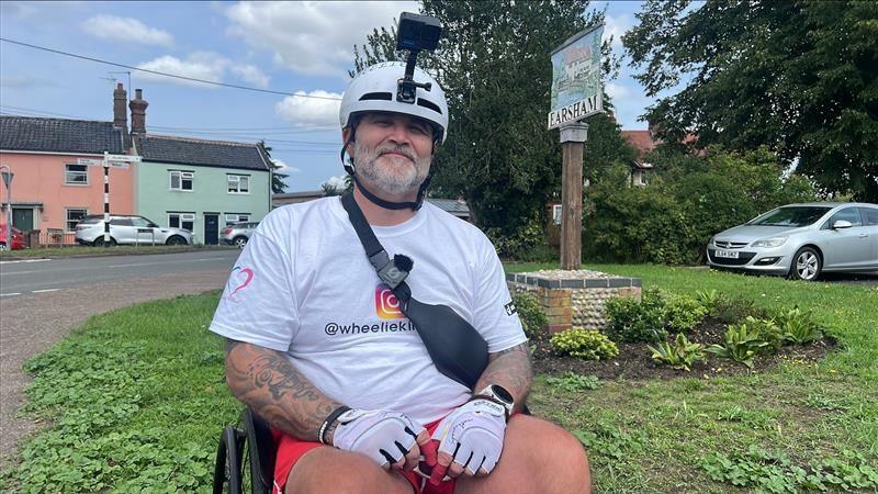 A wider view of Mr Parker in his wheelchair in a village centre.