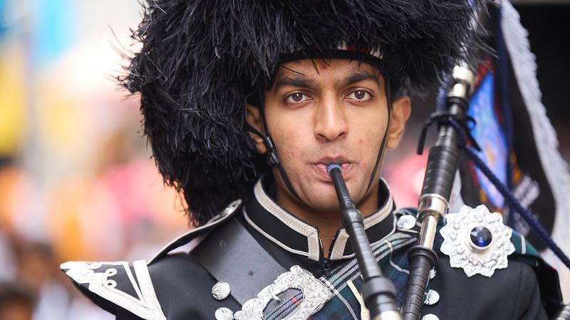 A man playing the bagpipes in traditional headdress and uniform