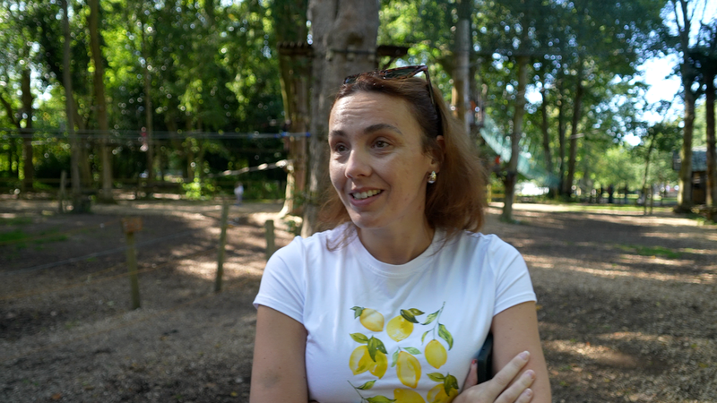 Rachel standing with woodland in the background wearing a white t shirt with yellow lemons on the front with her arms folded 