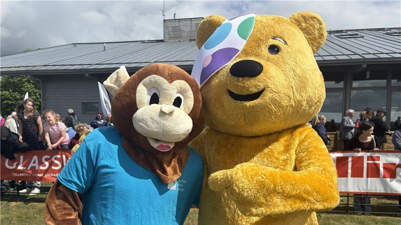 Two people wearing mascot costumes pose at the camera. One of the costumes is a monkey wearing a blue T-shirt and the other is the BBC's Pudsey Bear who is yellow with a polka dot bandage over one eye. 