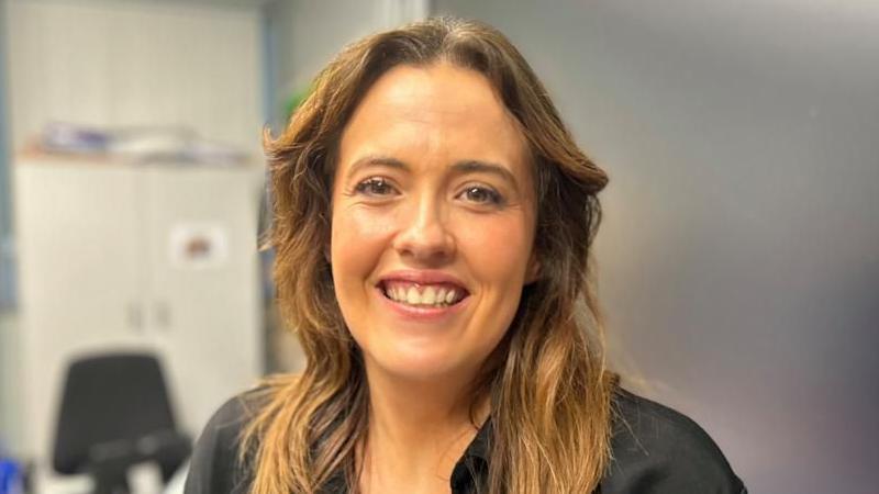 Tahnee is smiling at the camera and has long light brown hair. She is wearing a black blouse.