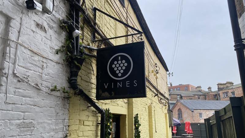 The outside sign of Vines bar, located in Sadler Gate in Derby, with its brick exterior painted in all yellow