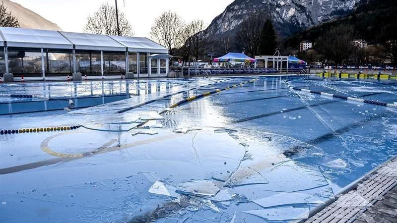 Ice over the pool where the competition takes place. Chunks of broken ice can be seen all over the frozen water. A snowy mountain can be seen in the background.