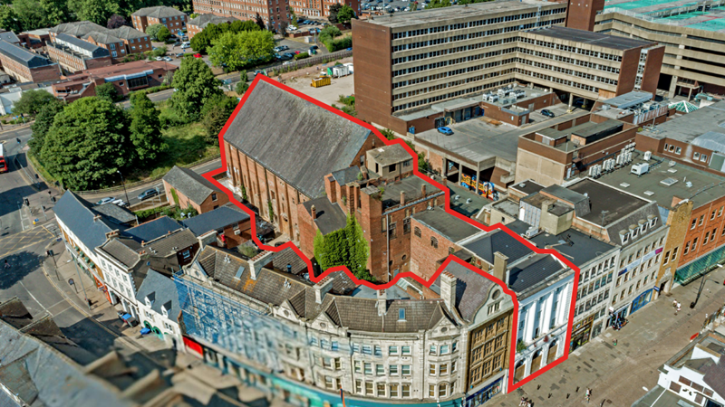 Three-storey buildings in a town centre at a curved intersection between two streets. The Corn Exchange site has a white entrance, and a large brick hall at the rear.