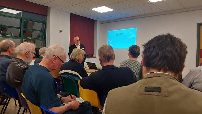 Richard Gibson, stakeholder manager West & Wales for CrossCountry, gives a presentation at a community meeting at West Oxford Community Centre on Botley Road in Oxford. He is in front of residents and campaigners. A screen behind him reads "Questions"