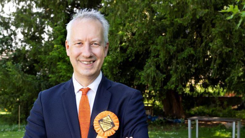 Gideon Amos wearing an orange rosette and matching tie