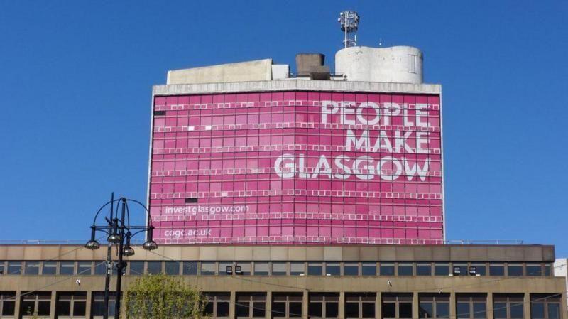 A big tower, with a large pink graphic saying PEOPLE MAKE GLASGOW over the top.