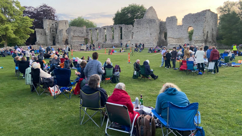 A ruined stone building surrounded by scores of people sitting in picnic chairs.