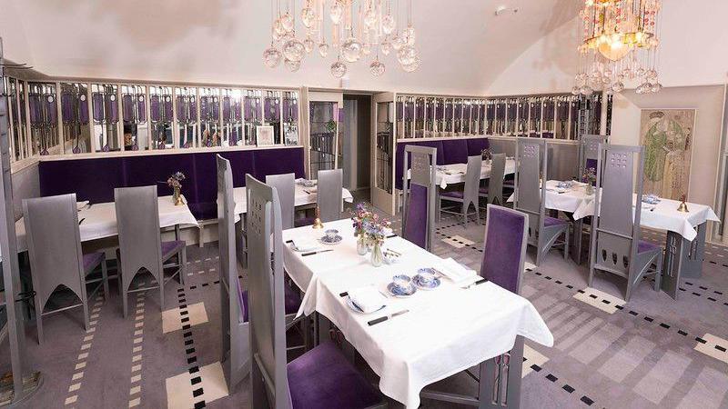 The inside of the tearooms is like a restaurant. There are 3 tables along the back with booths and two chairs at each of those tables. Then there are two tables in the middle with four chairs around each of them. The chairs are silver with purple cushions. The tables have white table clothes on them.