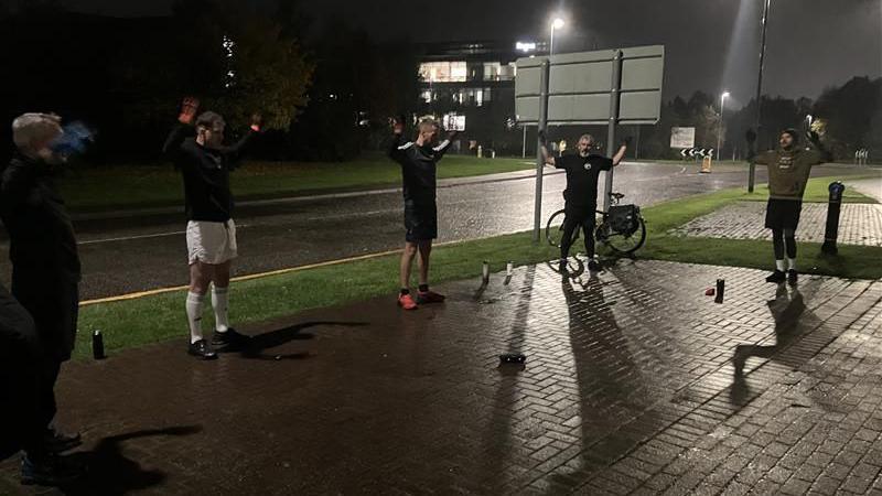 A few of the group members exercising. It is dark and the road is wet. There is a bicycle behind one of the men.  