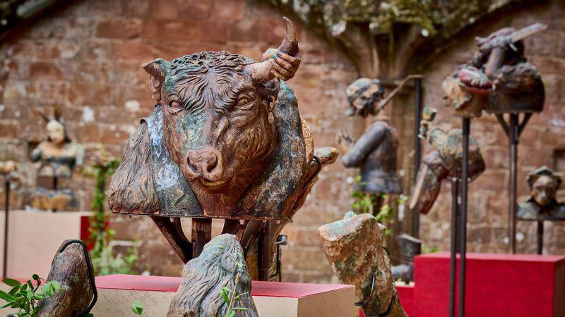A bust of a bull's head in an outdoor area with a red brick wall, with other statues surrounding it