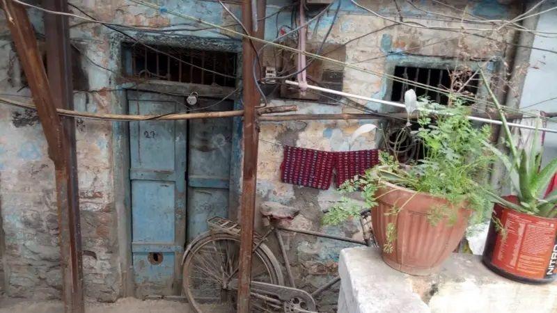 A photo showing a broken blue door to a rundown room with pain peeling off its walls