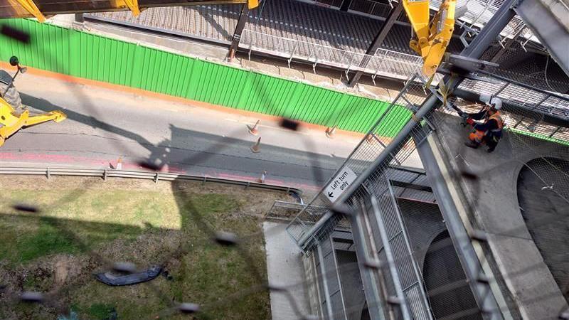 A worker wearing an orange hi-vis jacket is assessing the damage on an upper level of the car park. There is debris on the floor. A metal barrier is hanging off the end of the car park where the worker is.