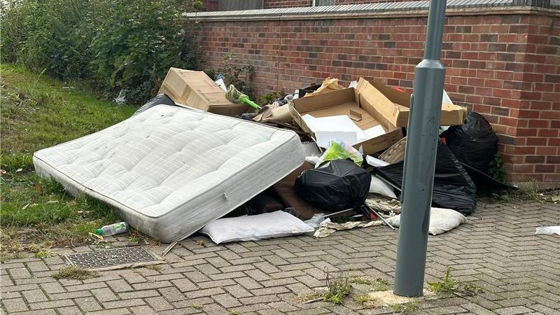 A dirty mattress, cardboard boxes and black bin bags piled up on the corner of a pavement.