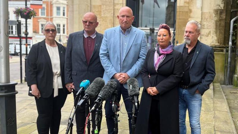 Five people standing in front of microphones outside a court building