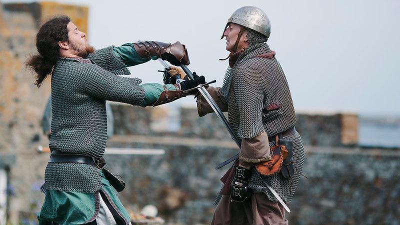 Two men in chainmail demonstrate sword fighting.