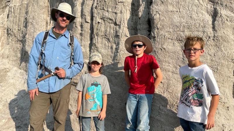 Three young boys and an adult at the excavation site in sunny weather